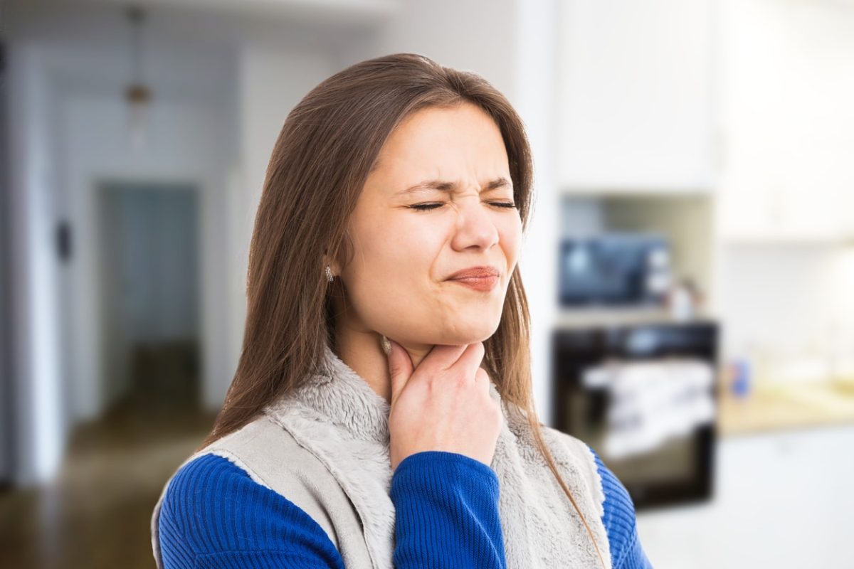 Woman holding her sore throat looking uncomfortable